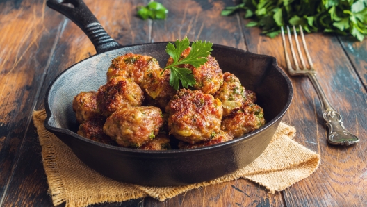 Homemade roasted beef meatballs in cast-iron pan on wooden table in kitchen.