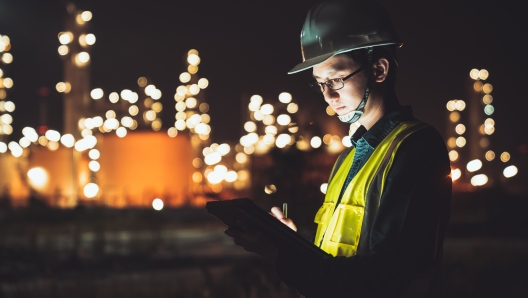 Asian man engineer using digital tablet working late night shift at petroleum oil refinery in industrial estate. Chemical engineering, fuel and power generation, petrochemical factory industry concept