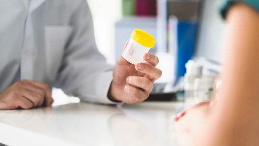 Doctor, patient and urine test cup. Physician giving pee container to a woman in clinic or hospital emergency room. Urinary sample for medical exam in hospital. Checkup for infection or salmonella.