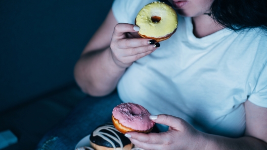 Emotional eating, mental disorder, depression, loneliness, stress. Lonely woman eating sweets and watching tv late in the night. Nerve food