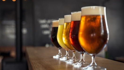 Glasses with different sorts of craft beer on wooden bar. Tap beer in pint glasses arranged in a row. Closeup of five glasses of different types of draught beer in a pub.