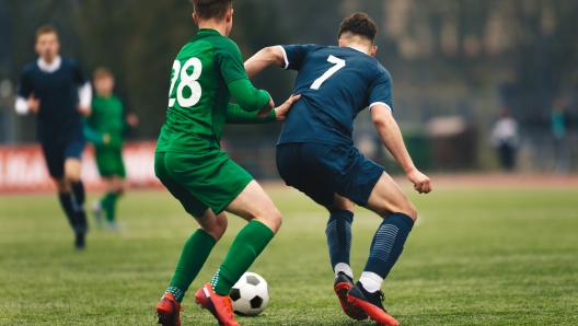 Adult football competition. Soccer football player dribbling a ball and kick a ball during match in the stadium. Footballers in action on the tournament game