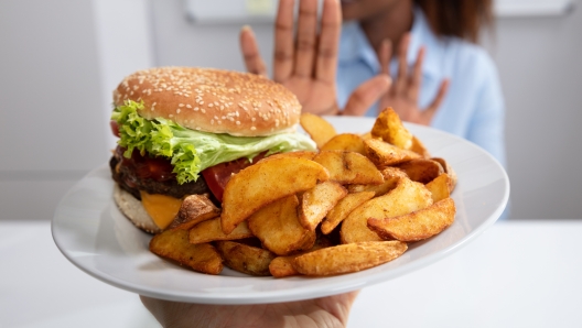 Young Woman Refusing Burger And French Fries On Plate