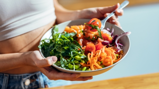 Shot of fitness woman eating a healthy poke bowl in the kitchen at home.