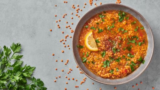 Red lentils tomato soup with parsley and lemon in gray plate on concrete table top. Vegetarian dish. Copy space