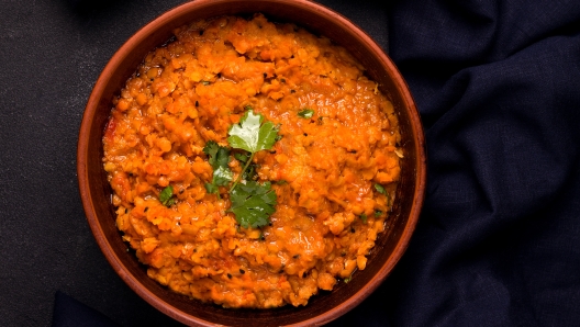 Dhal traditional vegetarian red lentil bean soup with cilantro on a black background.