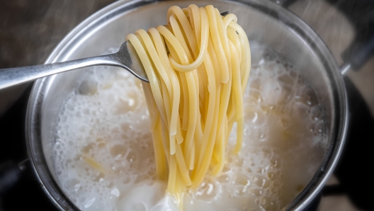 Yellow noodles or spaghetti cooking in boiling water pot with indoor low lighting.