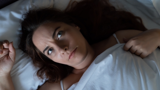 Depressed young woman dont sleep at night, lying on bed, looks up and suffers from insomnia, top view.