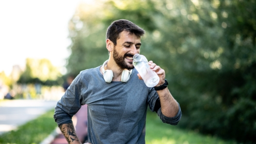 A young skinny Caucasian male is resting on a treadmill and drinking water