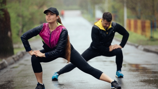 Two friends sportsmen stretching and warming up at rainy day