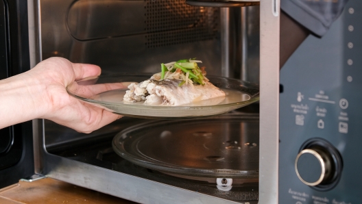 A housewife steaming fish in a microwave oven for a family dinner. She prepares it by putting fish dishes in the microwave and then serving healthy food. Cooking ideas