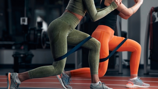 Sporty women in gym exercising with elastic resistance rubber band.