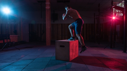 Muscular man training wooden box pacing in dark gym. Athlete workout in red blue neon light. Healthy lifestyle cross training