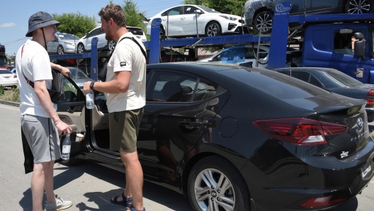 Russian Yaroslav Kolchenko (R), 31, used car dealer, and his friend inspect a car they bought for resale in the Armenian town of Gyumri on July 20, 2023. A kilometres-long caravan of trailers loaded with used cars meanders on a dusty road leading to a customs terminal in the Armenian city of Gyumri. While the US and the EU have banned the export of vehicles to Russia, cars can still be exported through Armenia and 31-year-old Russian used car dealer Yaroslav Kolchenko stands to gain. "There is a car drought, dealers without cars," he tells AFP. "This scheme, in a nutshell, is today the only way by which cars enter Russian territory." (Photo by Karen MINASYAN / AFP)