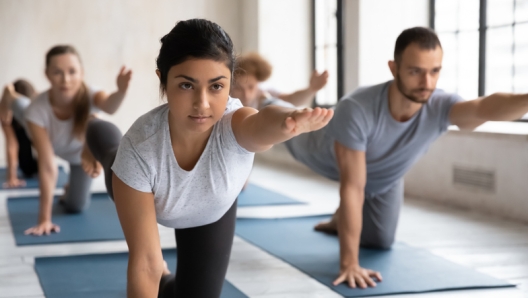 Serious focused Indian ethnicity female yoga instructor and group of young people performing Parsva Balasana Bird Dog Pose during workout at sport club studio. Strengthens core and low back exercise