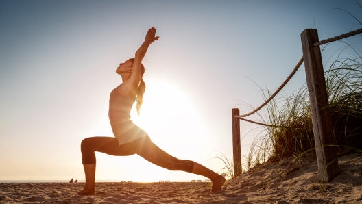 Woman performs stretching exercises on a beach at sunrise