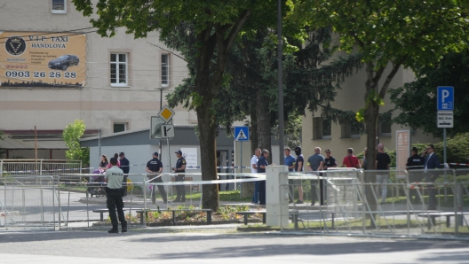 epa11342303 Police officers and onlookers stand near the cordoned-off crime scene where Slovak Prime Minister Robert Fico was shot earlier in the day, in Handlova, Slovakia, 15 May 2024. According to a statement from the Slovak government office on 15 May, "following a government meeting in Handlova, there was an assassination attempt on the Prime Minister of the Slovak Republic Robert Fico. He is currently being transported by helicopter to Banska Bystrica Hospital in a life-threatening condition."  EPA/JAKUB GAVLAK