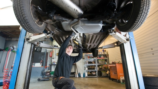 A mechanic is checking the exhaust of a car who is lifted up in a repair service station.