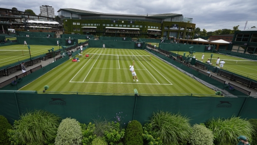 Tennis players train as a member of ground staff waters the plants at the All England Lawn Tennis and Croquet Club in Wimbledon, London, Friday, June 28, 2024. The Wimbledon Championships begin on July 1. (AP Photo/Kirsty Wigglesworth)