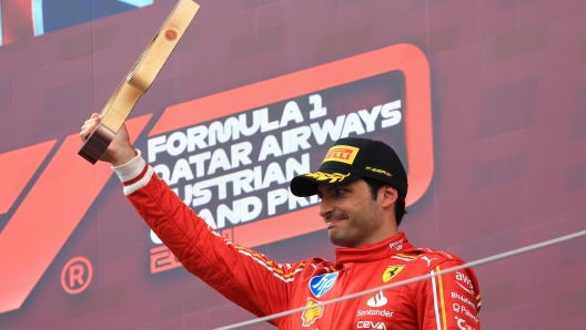 epa11447438 Scuderia Ferrari driver Carlos Sainz Jr. waves on the podium after placing third in the Formula One Austrian Grand Prix, in Spielberg, Austria, 30 June 2024.  EPA/MARTIN DIVISEK