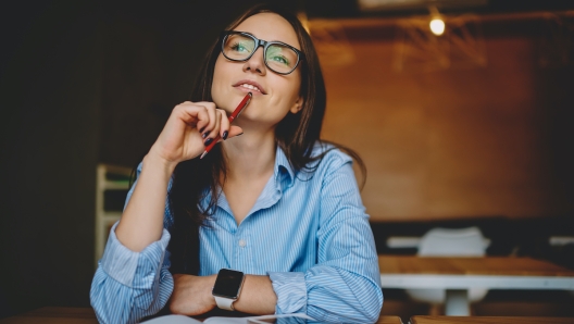 Dreamy woman podring while working on journalistic publication sitting with notebook in cafe,thoughtful female student in eyewear doing homework task solving problems and analyzing information