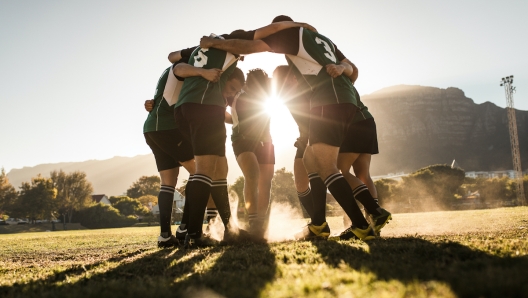 Rugby team standing in a huddle and rubbing their feet on ground. Rugby team celebrating victory.