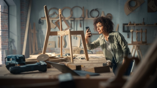 Artisan Product Designer Taking a Smartphone Photo of a Wooden Chair Project. Multiethnic Creative Female Uploading Picture Online to Her Social Media Profile for Feedback from Followers and Friends.