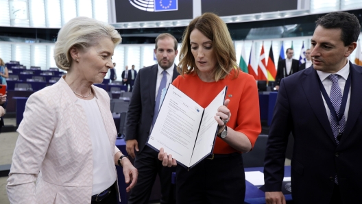 epa11485449 European Parliament President Roberta Metsola (C) shows the appointment documents to Ursula von der Leyen (L) after being re-elected as European Commission President during a plenary session of the European Parliament in Strasbourg, France, 18 July 2024. MEPs re-elected Von der Leyen as European Commission President for the next five years.  EPA/RONALD WITTEK