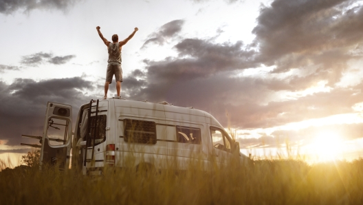 Man with raised arms on top of his camper van