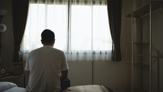 Silhouette depressed man sadly sitting on the bed in the bedroom. Sad asian men suffering depression insomnia awake and sit alone on the bed in bedroom. Depression health people concept.