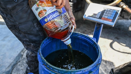 A worker pours a bottle of used cooking oil to be recycled into biodiesel at a food shop on the Malaysian resort island of Langkawi on February 29, 2024. (Photo by Mohd RASFAN / AFP)