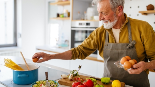 Happy retired mature man cooking in kitchen. Retirement, hobby people concept