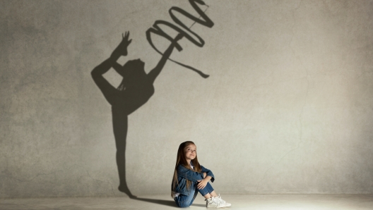 Baby girl dreaming about gymnast profession. Childhood and dream concept. Conceptual image with shadow of female gymnast on the studio wall