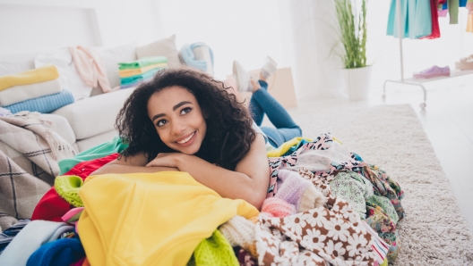 Full size photo of pretty young woman lying messy pile stack clothes fantasize apartment indoors.