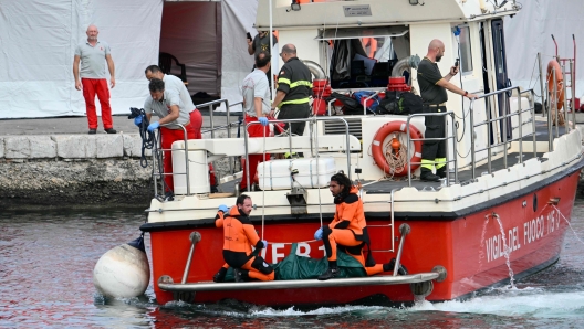 Divers of the Vigili del Fuoco, the Italian Corps. of Firefighters arrive with a body bag at the back of the boat in Porticello near Palermo, on August 21, 2024 two days after the British-flagged luxury yacht Bayesian sank. Rescuers with divers and an underwater drone search for six people believed trapped when the boat sank. Among the six missing were UK tech entrepreneur Mike Lynch and his 18-year-old daughter Hannah, and Jonathan Bloomer, the chair of Morgan Stanley International, and his wife Judy. The Bayesian, which had 22 people aboard including 10 crew, was anchored some 700 metres from port before dawn when it was struck by a waterspout, a sort of mini tornado. Fifteen people aboard, including a mother with a one-year-old baby, were plucked to safety; one man has been found dead; and six people remain missing. (Photo by Alberto PIZZOLI / AFP)