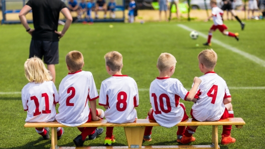 Children Soccer Team Watching Football Match. Children Sport Team in White Shirts. Youth Soccer School Tournament for Children. Young Boys in Soccer Jersey. Football Wooden Bench