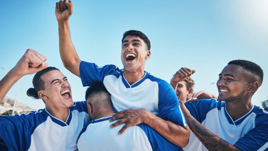 Football player, winner team and people winning in competition, game or sports goals, success and cheers. Yes, wow and excited group of young men with achievement and soccer celebration on blue sky