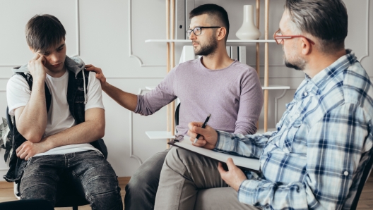 Young man in glasses comforting his depressed friend during meeting with counselor