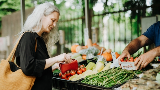 Portrait of a beautiful mature woman shopping at market in the city. Middle-aged woman buying fresh vegetables and fruits from market stall.