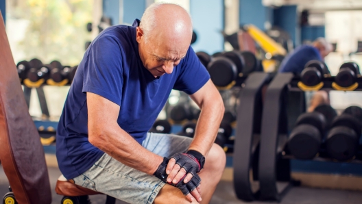 A portrait of bald senior man feeling strong knee pain during training in the gym. People, healthcare and lifestyle concept