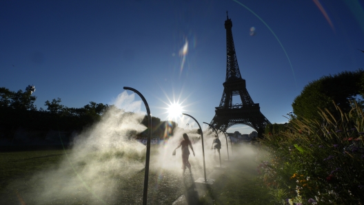 A spectator walks through a water mist sprayer on her way to the Eiffel Tower Stadium to watch a beach volleyball match at the 2024 Summer Olympics, Sunday, July 28, 2024, in Paris, France. (AP Photo/Robert F. Bukaty)