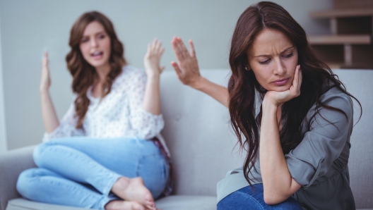 Two female friends sitting on sofa and arguing with each other