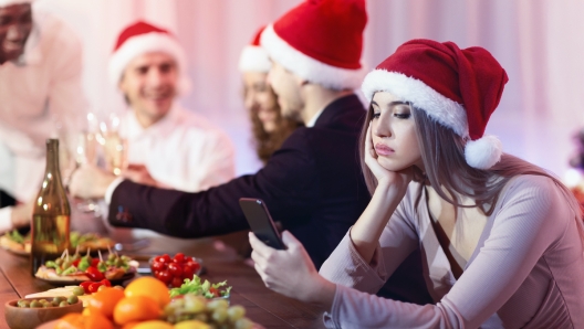 Boring New Year Party. Sad Girl Texting On Phone During Dreadful Christmas Dinner With Friends Sitting At Celebratory Table Indoor