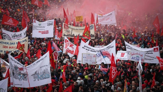 Employees of German automobile manufacturer Volkswagen display banners and flags during a demonstration called for by metalworkers' union IG-Metall at the Volkswagen Plant in Wolfsburg, northern Germany, on November 21, 2024, during a third round of negotiations between management and workers' representatives on a new deal for the crisis-hit company. Auto giant Volkswagen will face strikes of a magnitude unseen in Germany for decades unless it rules out plant closures, a union warned on November 20, ahead of fresh talks. The union representing workers at Europe's biggest carmaker also presented proposals it said would save 1.5 billion euros (USD 1.58 billion) in labour costs without the need for drastic steps. The crisis at the carmaker, facing problems ranging from high costs to slowing sales in China, erupted in September when it said it was mulling the closure of factories at home in Germany for the first time. Ahead of negotiations, the IG Metall union urged management to heed their suggestions and drop their most dramatic plans. (Photo by Ronny HARTMANN / AFP)