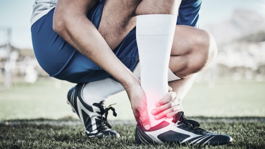 Injury, sports and hand of a man on foot pain, soccer emergency and accident while training. Fitness, problem and  an athlete or football player with inflammation or a swollen muscle on the field