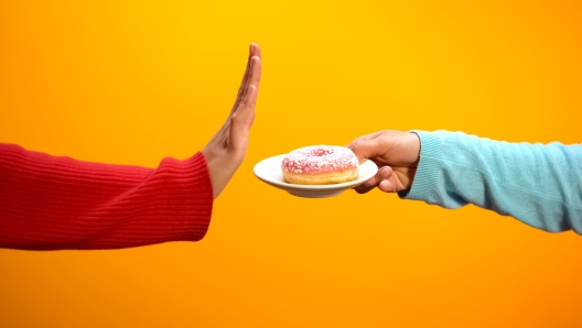 Hand showing stop sign rejecting glazed donut on bright background, weightloss