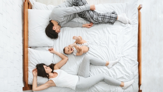 Joint sleep with kids. Exhausted parents sleeping on sides of bed, active baby playing in middle, above view