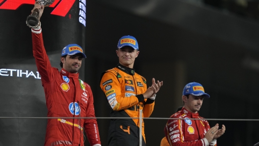 From the left, third-placed Ferrari driver Carlos Sainz of Spain, first-placed McLaren driver Lando Norris of Britain, and second-placed Ferrari driver Carlos Sainz of Spain stand on the podium after the Formula One Abu Dhabi Grand Prix at the Yas Marina Circuit in Abu Dhabi UAE, Sunday, Dec. 8, 2024. (AP Photo/Altaf Qadri)