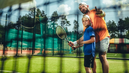 Portrait of concentrated male trainer teaching serene boy playing tennis outdoor. He pointing hand