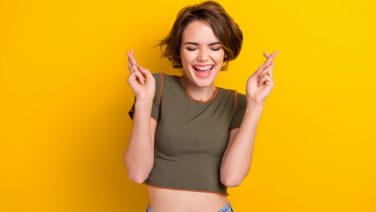 Photo of good mood adorable girl dressed stylish khaki t-shirt making wish laughing eyes closed isolated on yellow color background.